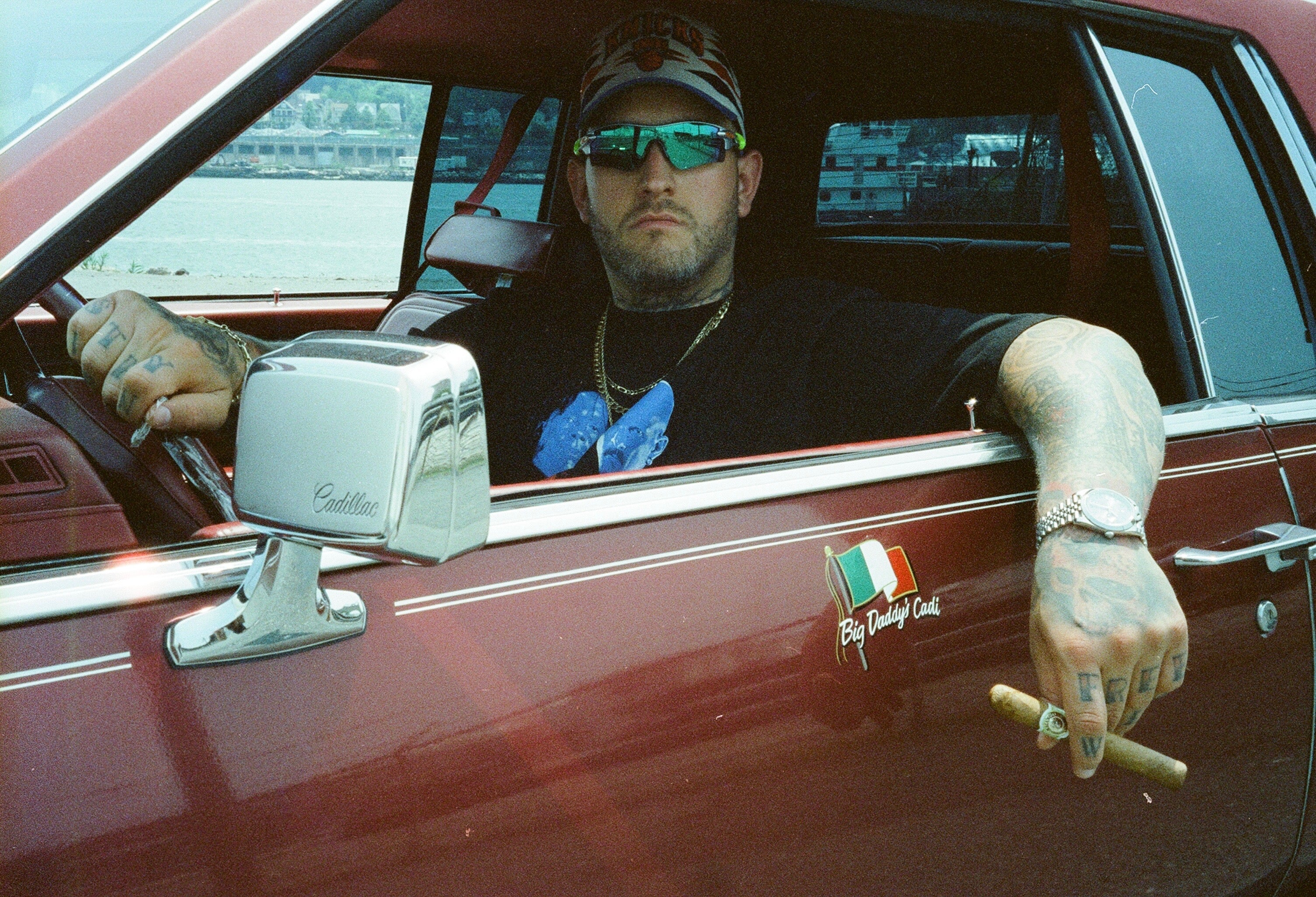 tattooed man in tank top holding bonsai tree outside